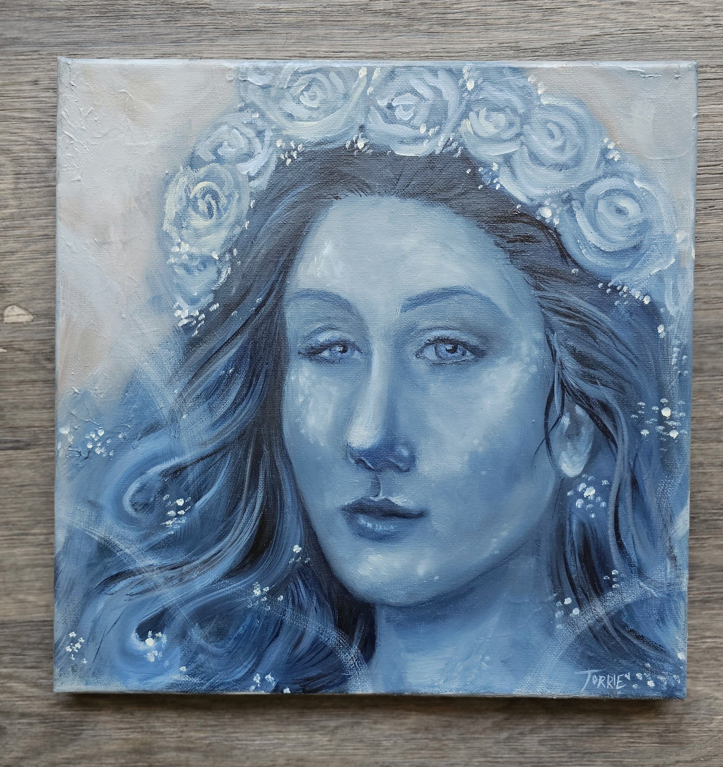 Painting of a woman's face with floral crown on a wooden surface