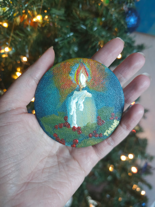 Hand holding a circular painted magnet with a Christmas tree in the background