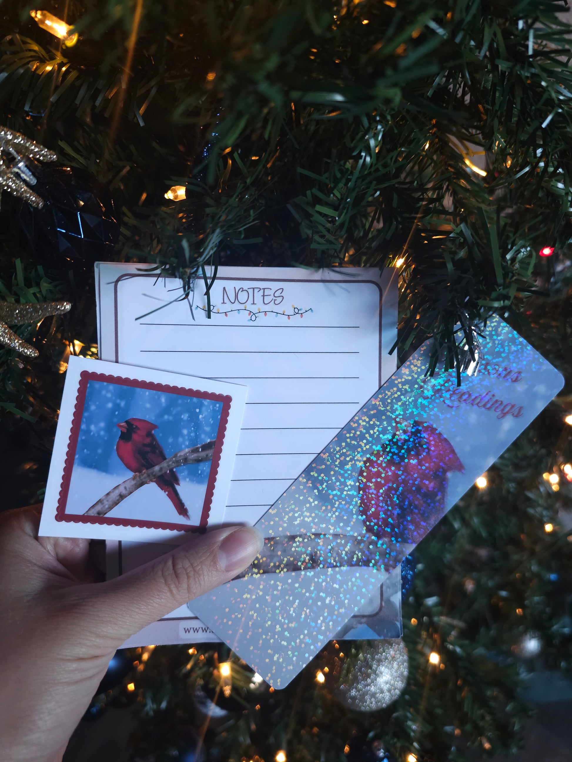 Hand holding a card with a red cardinal design in front of a decorated Christmas tree.