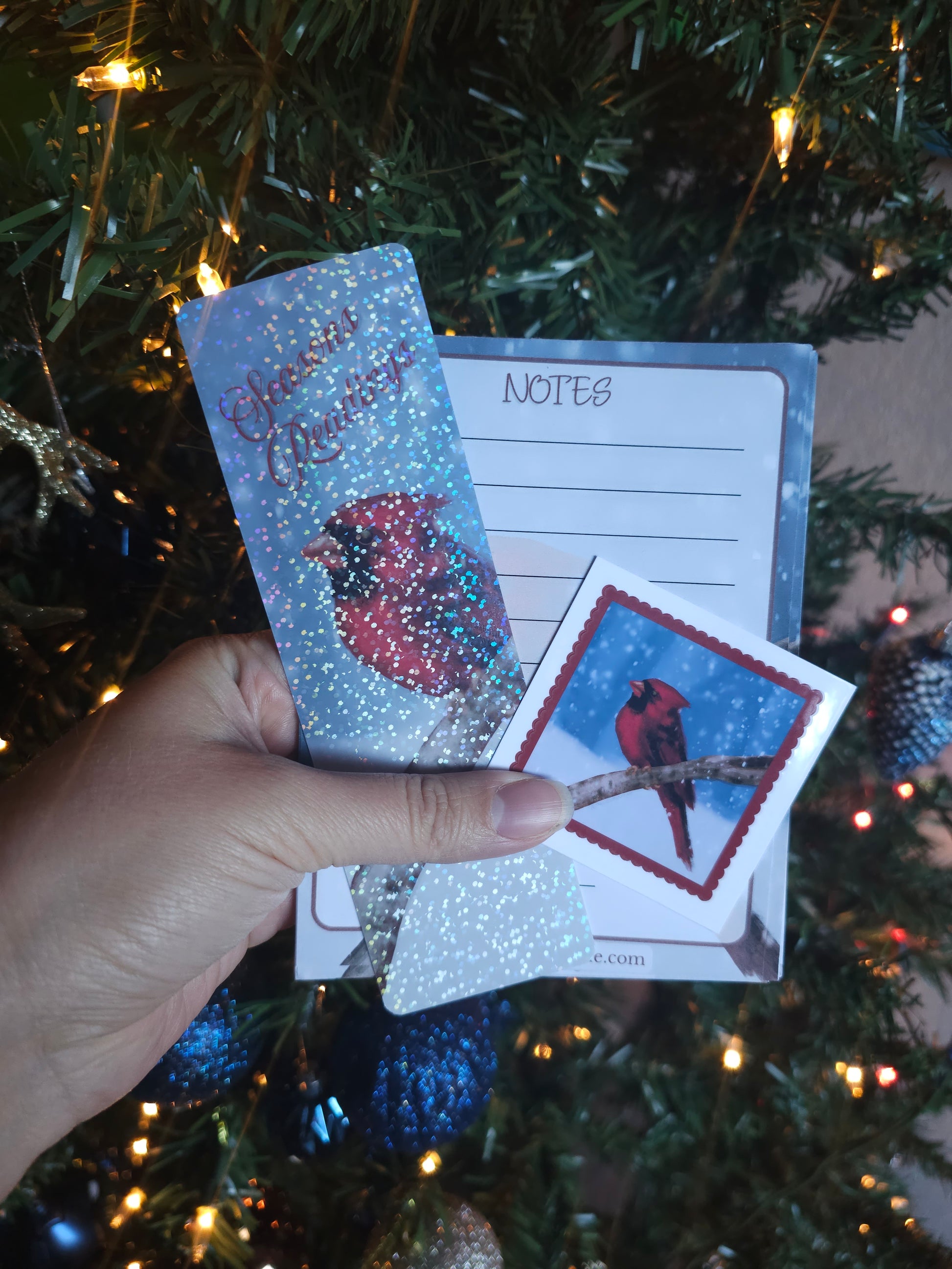 Hand holding Christmas cards with a decorative design in front of a decorated tree.